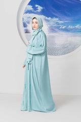 Elegant woman in light blue abaya stands by a circular window.