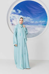 Woman in blue abaya posing in front of ocean backdrop