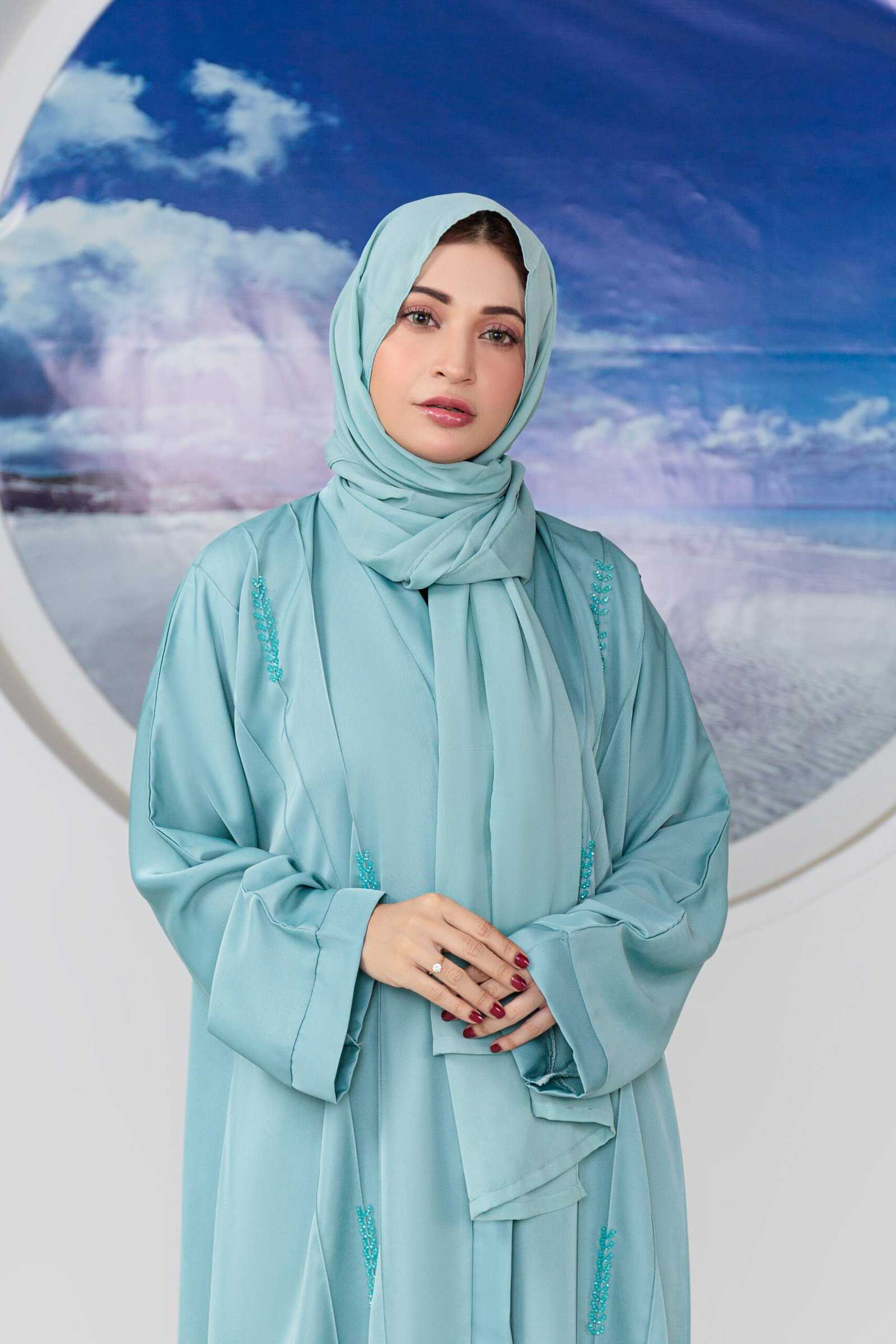 Woman in elegant turquoise hijab against ocean backdrop