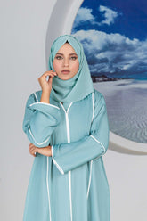 Woman in stylish teal hijab and dress by a beach backdrop