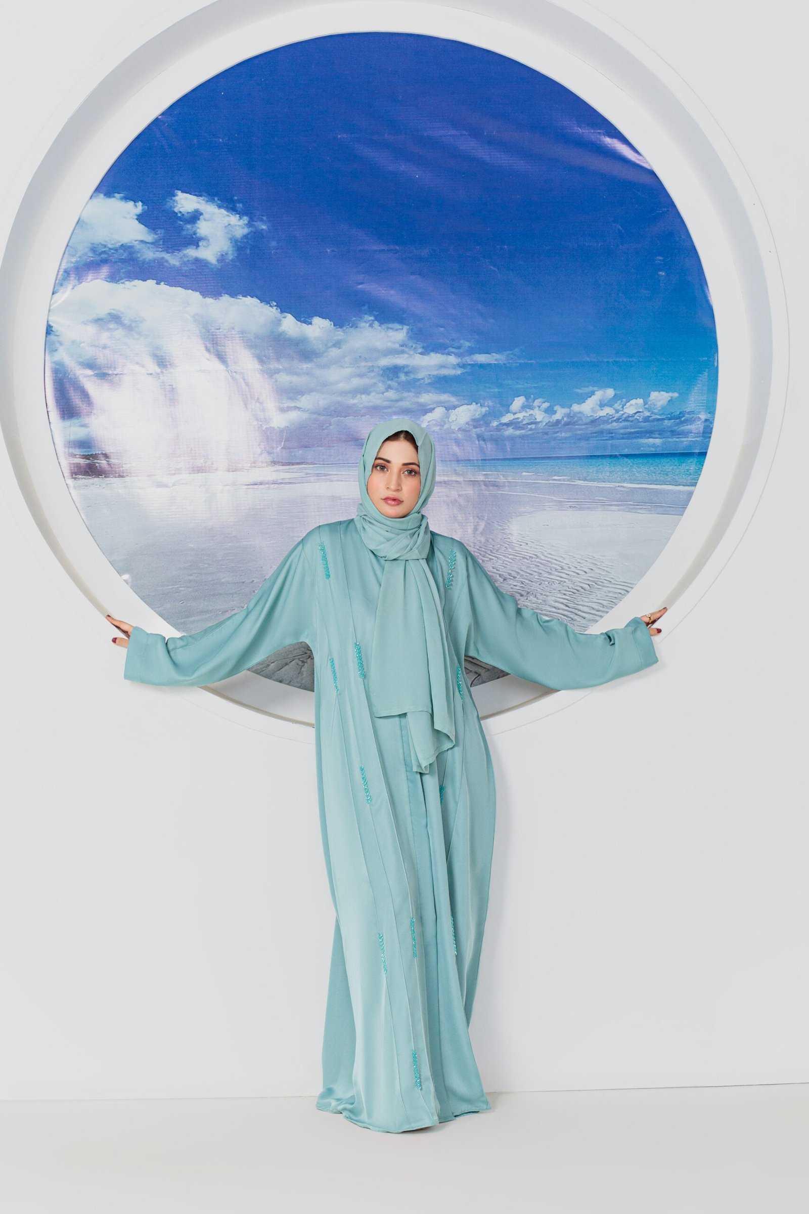 Woman in blue abaya standing by circular ocean backdrop