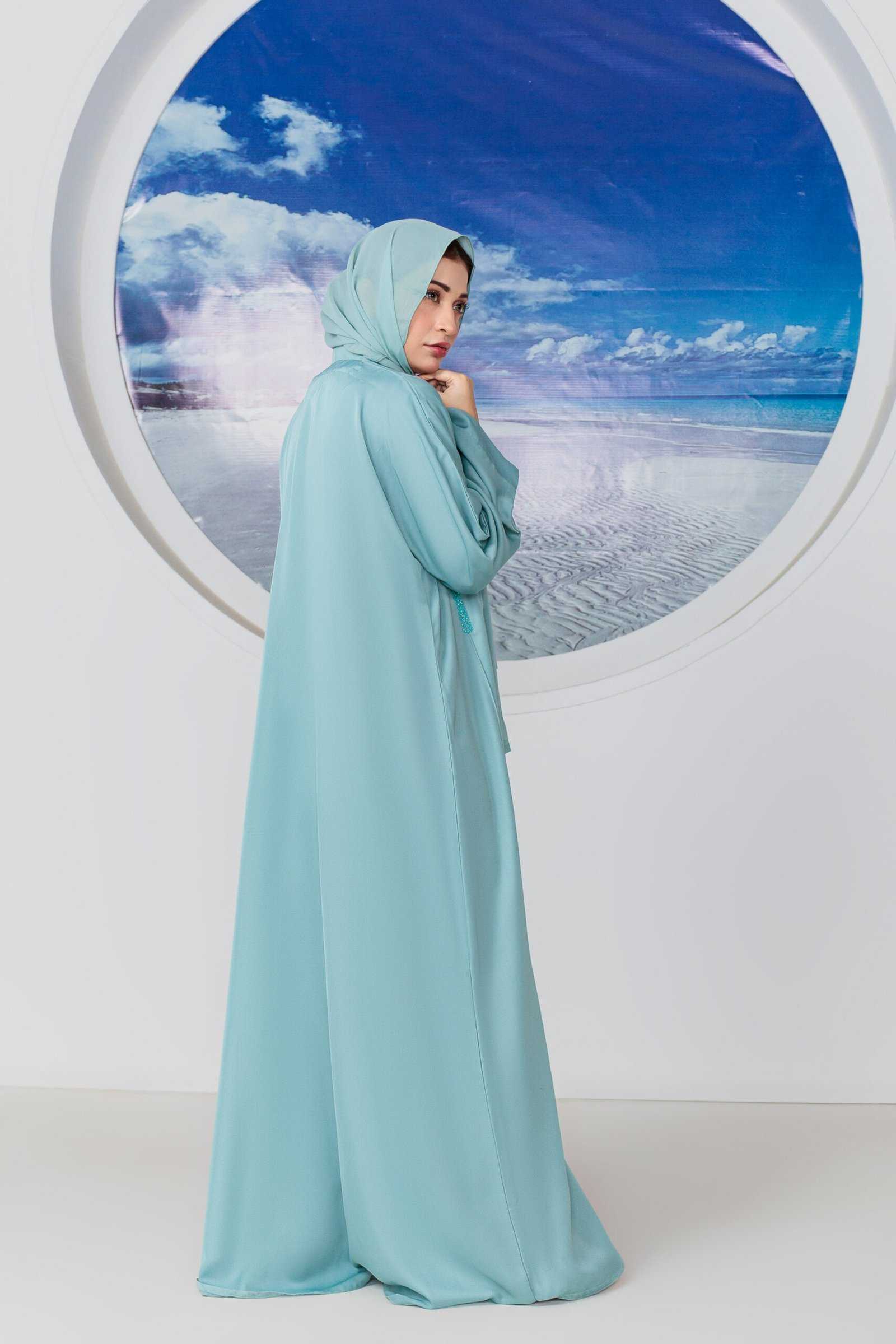 Woman in elegant blue abaya near beach-themed backdrop