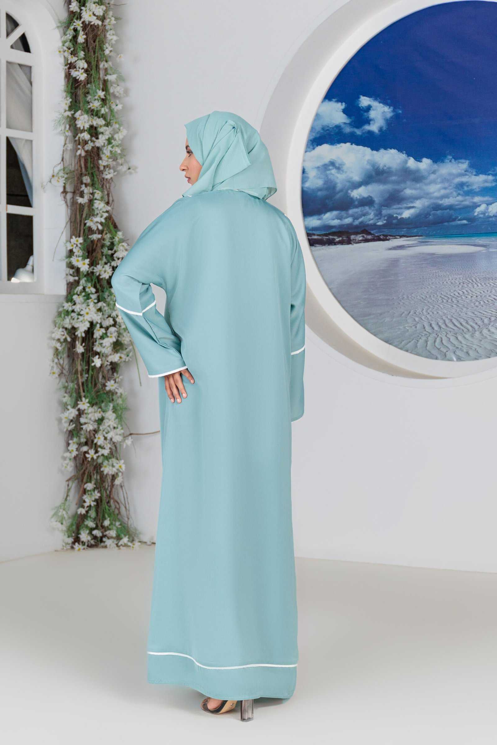 Woman in blue abaya posing indoors near scenic wall art